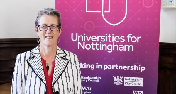 Dr Kathy McLean stands by a poster for Universities for Nottingham