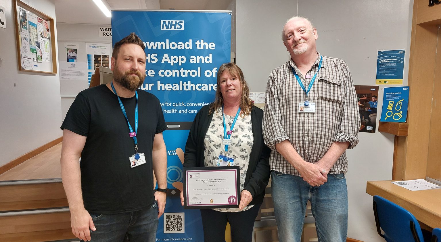 Three people stood infront of pull up banner showing award certificate