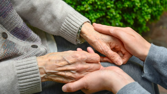 An elderly person holding hands with a younger person
