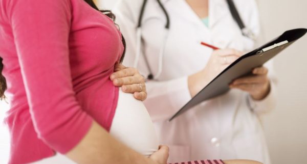 A pregnant woman chats to a doctor who is holding a clipboard