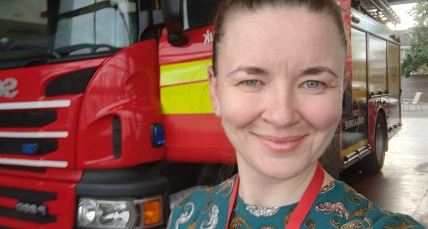 Photo of Rebecca smiling with a fire engine in the background