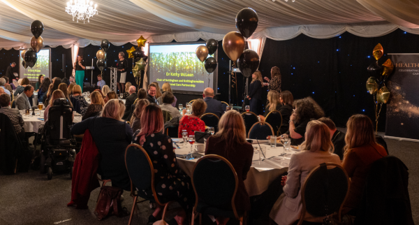 Photo of the awards ceremony with people sat at tables and the presenter on the stage