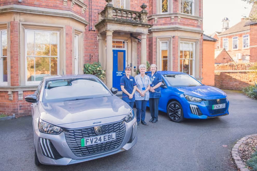 Three people stood outside Beaumond House with two cars side by side