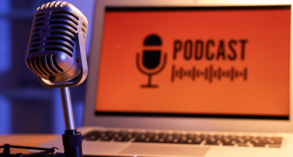 Photo of a microphone and a laptop with the word podcast on it